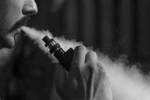 A man is using a vape to exhale smoke