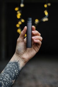 A man with a tattoo on his arm holds a vape